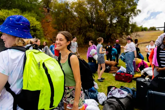 A camper with a bright backpack smiling at a friend on the lawn